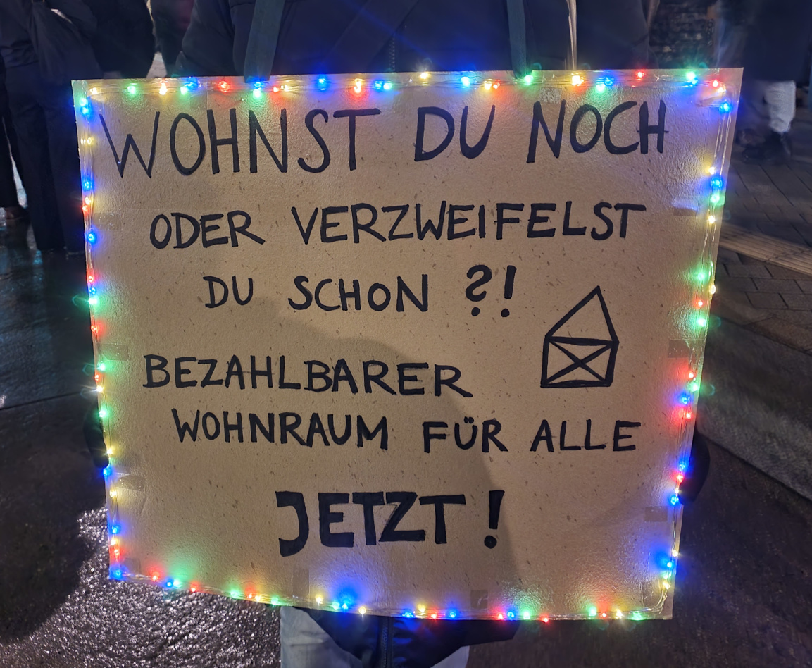 Demoplakat auf einer Demonstration gegen steigende Mieten. Auf dem Plakat steht: „Wohnst du noch oder verzweifelst du schon?! Bezahlbarer Wohnraum für alle – jetzt!"